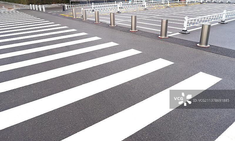 中国城市交通拍摄主题，逆光拍摄黑白相间的斑马线道路和不锈钢升降柱护栏，户外无人图像摄影图片素材