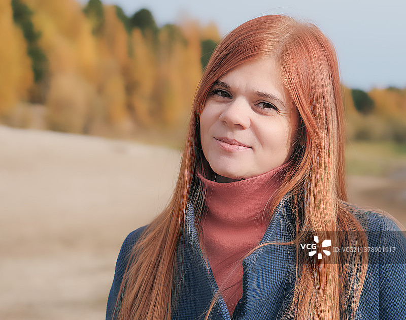 穿着外套坐在海边沙滩上的红发女人图片素材