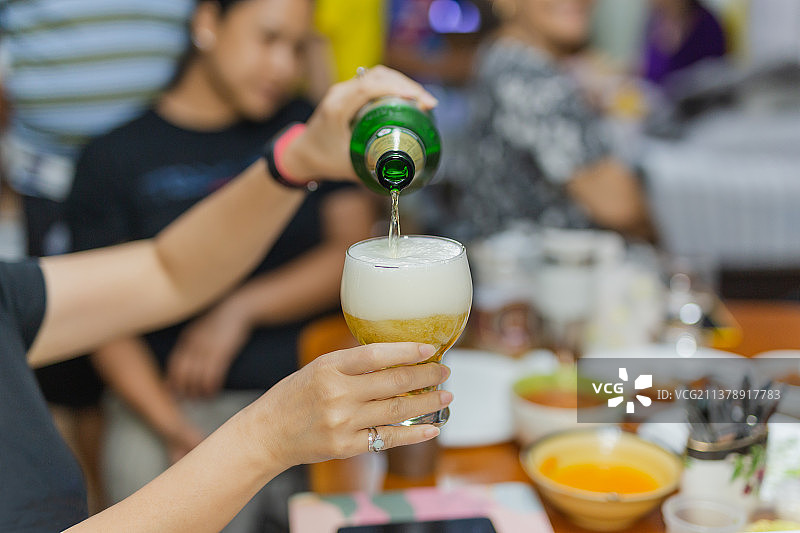 泰国：女人在家庭聚会倒瓶装啤酒入杯图片素材