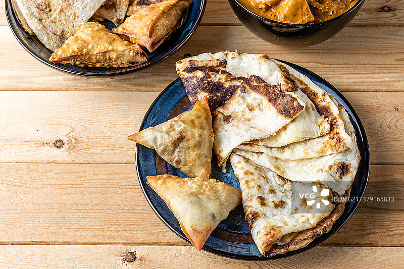 木桌上的印度小吃：萨摩萨三角饺、蒜蓉馕、黄油鸡图片素材