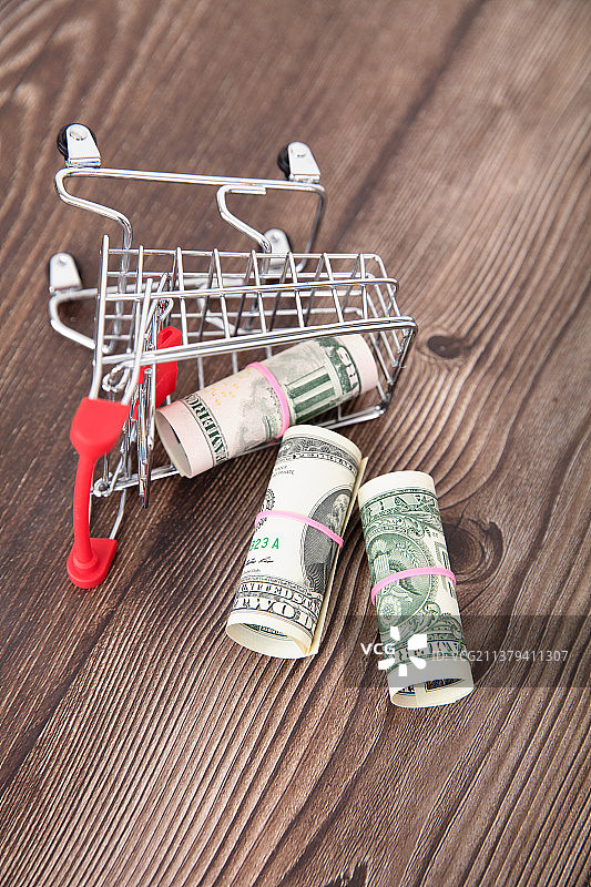 桌子上倾倒的购物车模型和散落的美元钞票图片素材