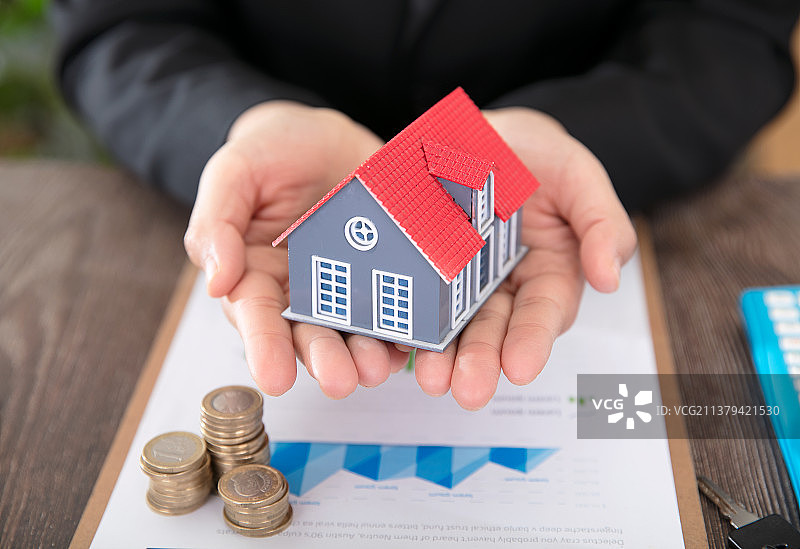 房地产相关从业者手捧小房子模型和相关文件与硬币图片素材