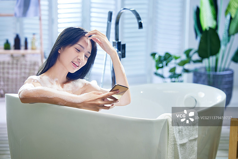 浴缸内使用手机的年轻女孩图片素材