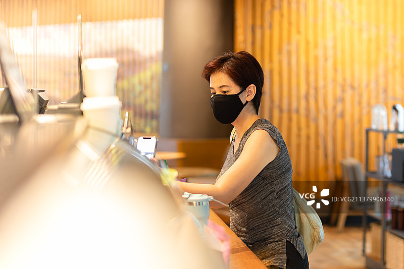 在泰国，戴防护口罩的女顾客在咖啡馆用手机支付账单图片素材