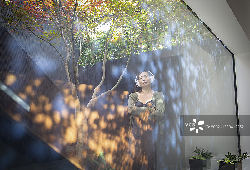 在庭院中戴着耳机，享受倒影的宁静女人图片素材