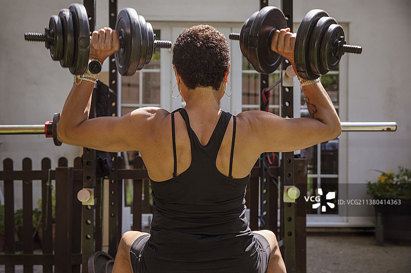 在后院用哑铃举重的健壮女人图片素材