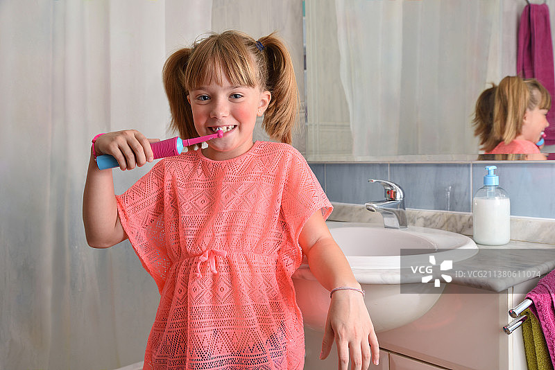 小女孩在浴室用电动牙刷刷牙。图片素材