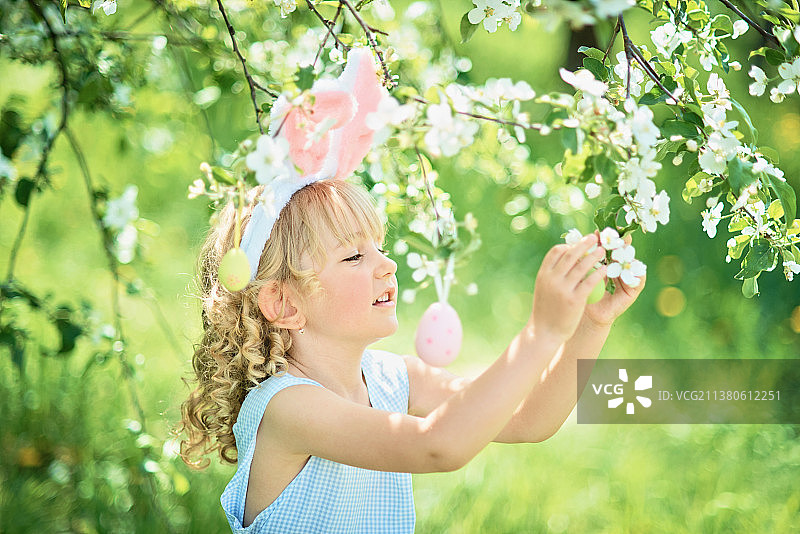 在花园里拿着复活节彩蛋和兔子耳朵的可爱女孩图片素材