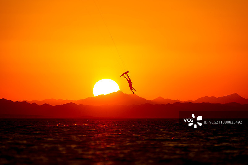 橙色天空下在海上玩尾波滑板的男子剪影图片素材