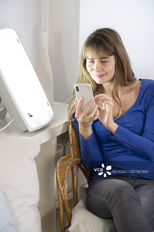 女人坐在光疗灯旁，拿着智能手机图片素材