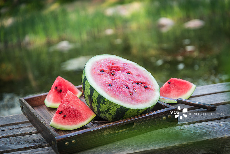 夏季户外水边木桌上切开的冰镇西瓜图片素材