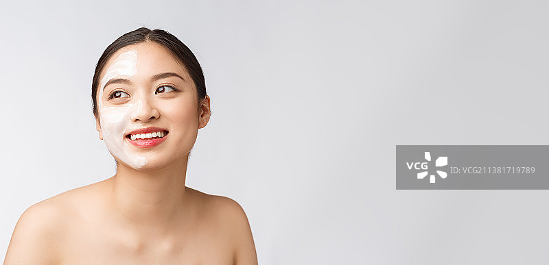 迷人而愉悦的女人在半边脸上涂抹乳霜图片素材