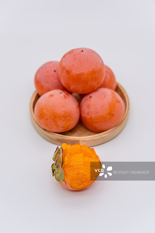 室内棚拍白背景前一盘新鲜的火晶柿子火柿子图片素材