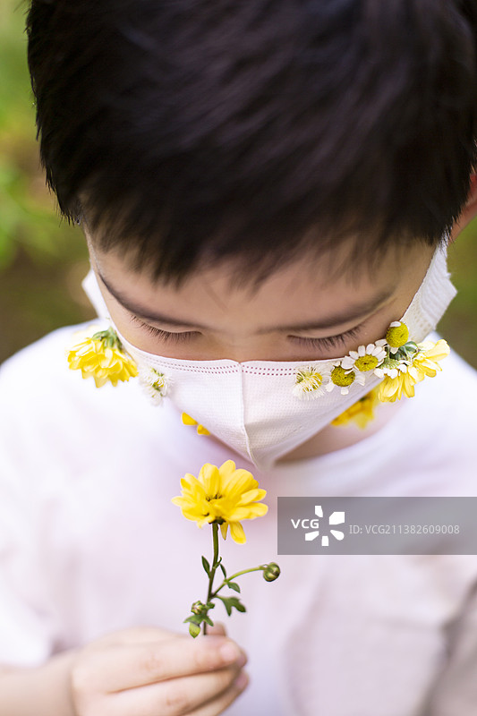 戴着插满鲜花口罩的小男孩闻着鲜花图片素材