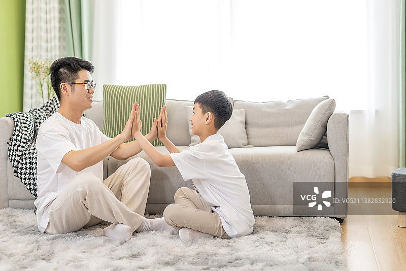 一对幸福的亚洲父子在客厅地毯上坐着图片素材