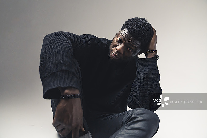 黑人男子坐着挠头，盯着白色相机图片素材