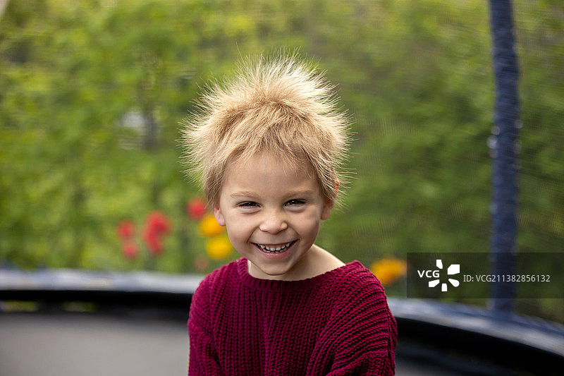 在蹦床上拍摄有趣肖像的可爱静电发小男孩图片素材