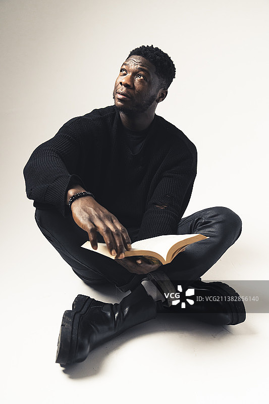 坐在白色背景前，手捧书本沉思的黑人男性图片素材