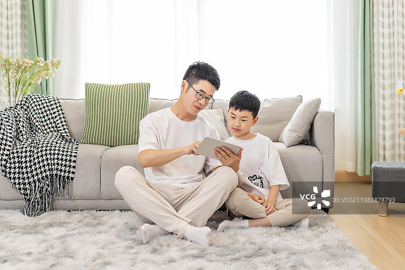 一对亚洲父子在客厅地毯上坐着使用平板电脑图片素材