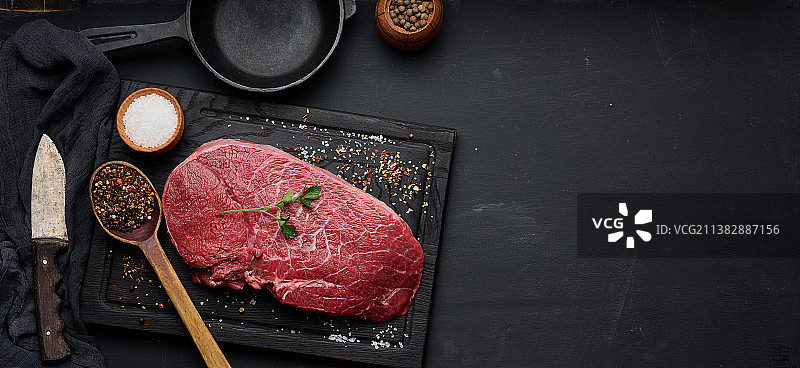 生牛里脊肉放在砧板上，黑色桌子上有烹饪用香料，顶视图图片素材