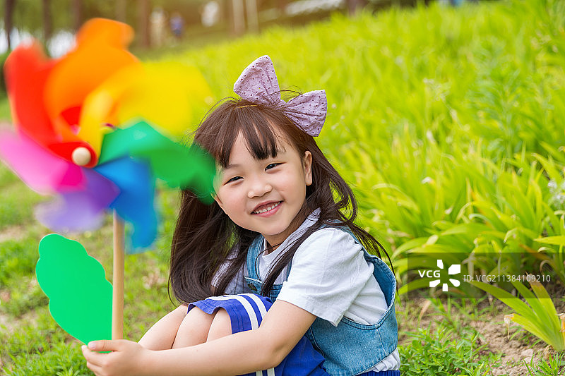 坐在草地上手拿风车开心的小女孩图片素材