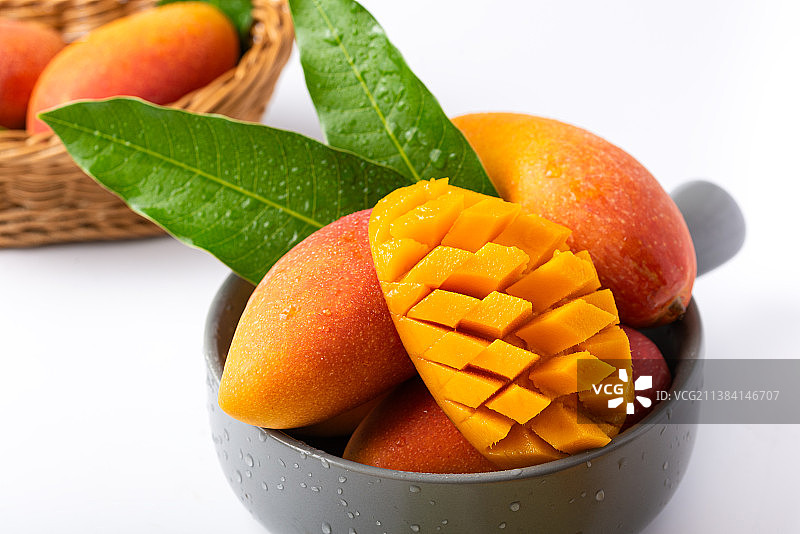 白底上灰色瓷碗盛装的新鲜芒果及切开的果肉图片素材