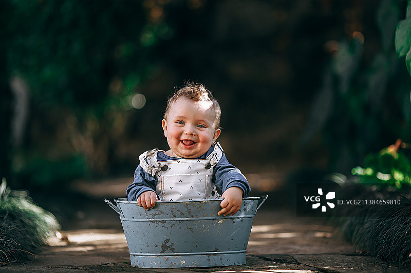 可爱的男婴在后院森林的锡桶里玩耍，巴西米纳斯吉拉斯州贝洛奥里藏特图片素材