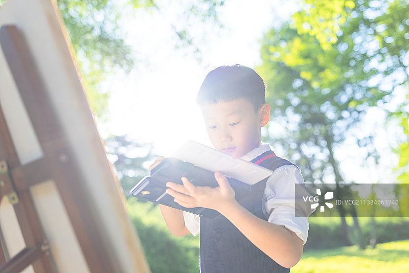 春天户外亚洲中国男孩手拿画笔在画板上画画图片素材