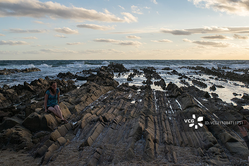 海滩日落时坐在岩石上的女子，拉帕洛马，罗恰省，乌拉圭图片素材