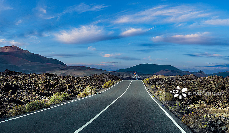 山地自行车手在通往山脉的空旷道路上的背影，西班牙拉斯帕尔马斯兰萨罗特岛图片素材