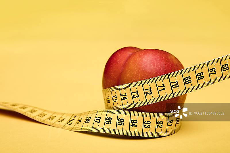 纤细身材，黄色背景上带卷尺的苹果特写图片素材