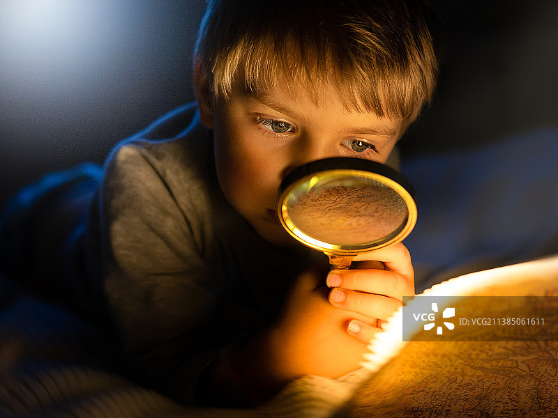 男孩在家躺在床上用放大镜看藏宝图特写图片素材