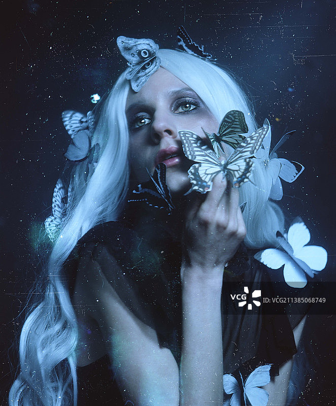 年轻女子在抽象的深色背景下手持纸蝴蝶图片素材