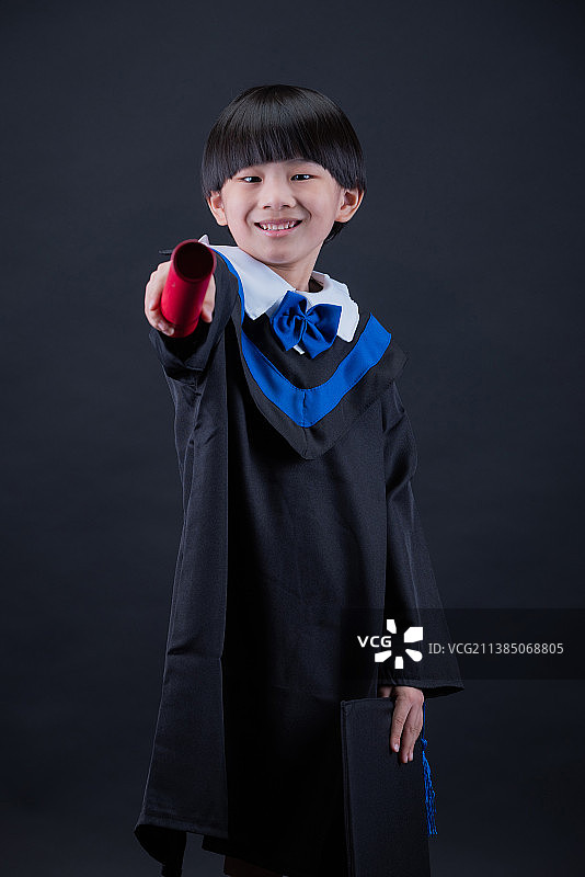 穿着毕业礼服站在黑色背景前的男孩肖像，马来西亚图片素材