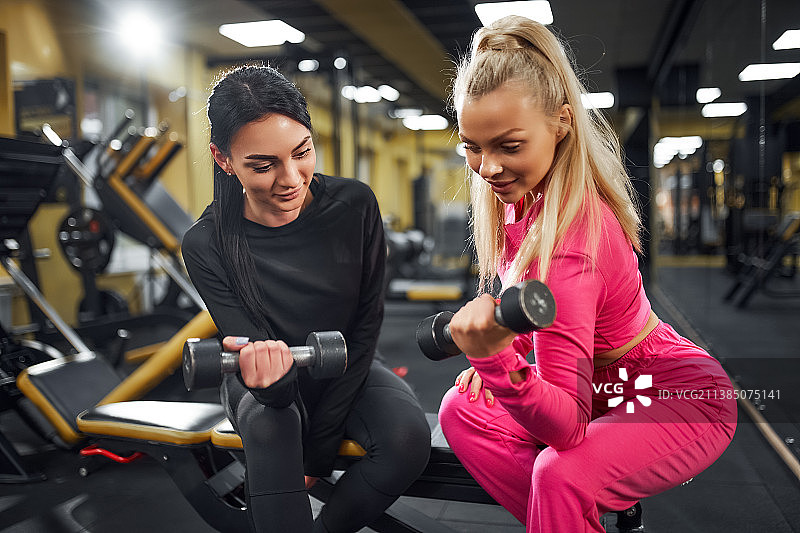 女教练向客户展示用哑铃锻炼肱二头肌的动作图片素材