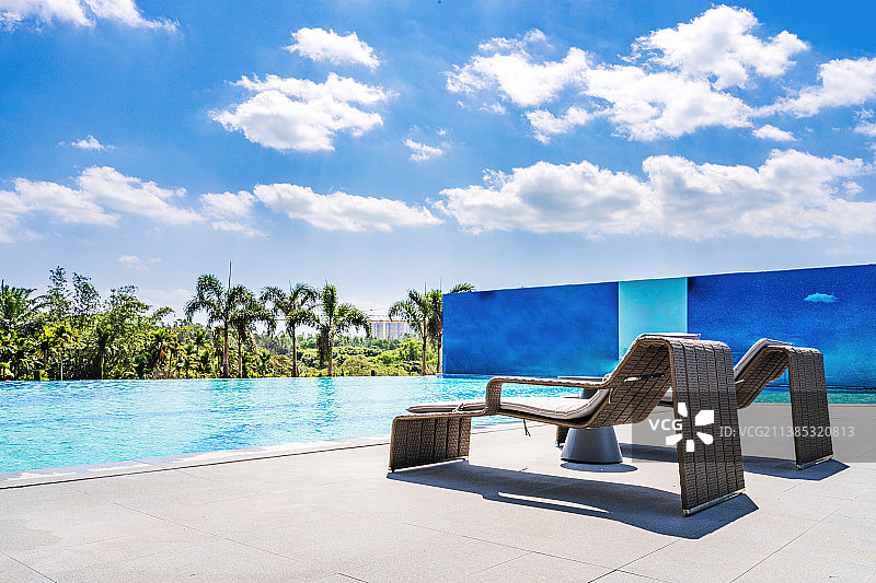 蓝天白云下的游泳池和泳池边的休闲躺椅图片素材