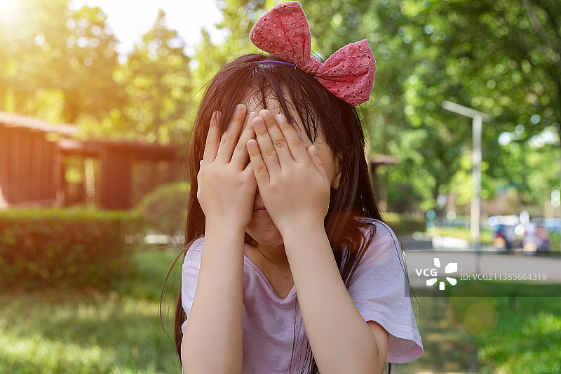 在公园里玩耍的亚洲小女孩双手捂脸图片素材