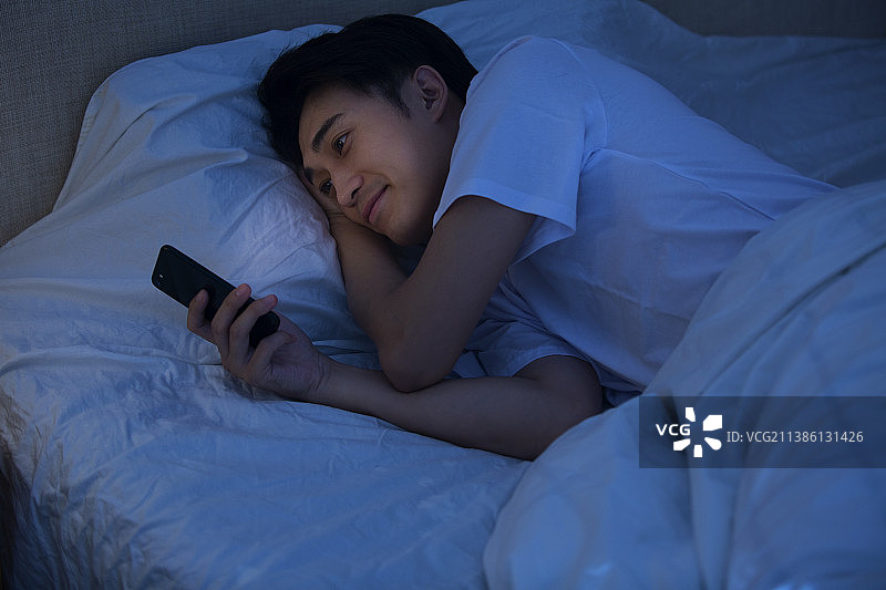 年轻男子深夜躺在床上玩手机图片素材