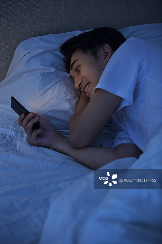 年轻男子深夜躺在床上玩手机图片素材