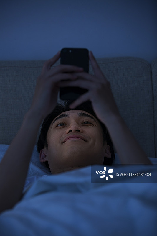 年轻男子深夜躺在床上玩手机图片素材