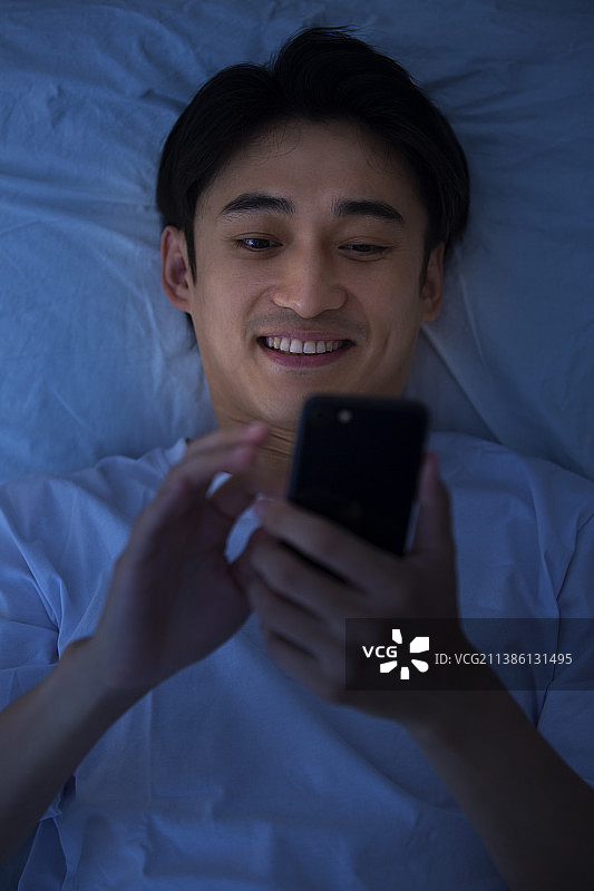 年轻男子深夜躺在床上玩手机图片素材