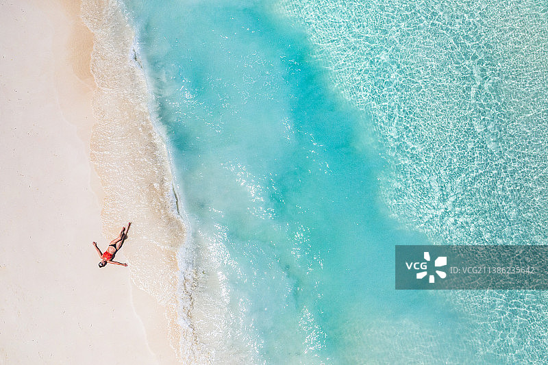 马尔代夫迪多菲诺卢岛南环礁，躺在海滩上的冲浪女孩鸟瞰图图片素材