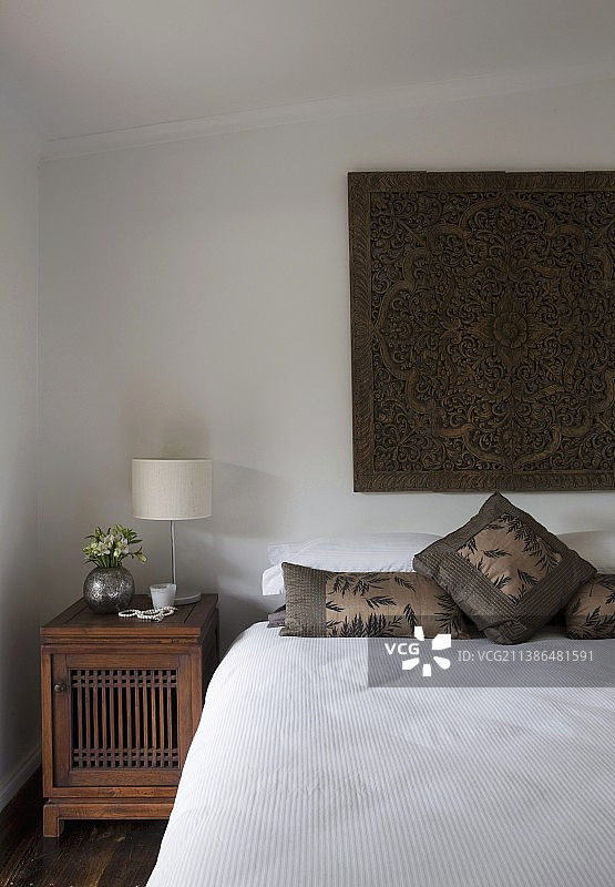 简约卧室，床上方有东方挂毯和古董木制床头柜图片素材