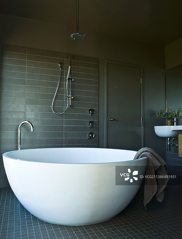男性浴室中，形状像半个蛋壳的独立式白色设计师浴缸图片素材