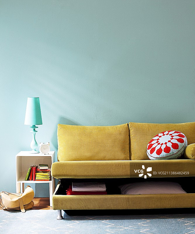黄棕色沙发床，半开式床上用品盒，搭配台灯和互补色墙壁图片素材