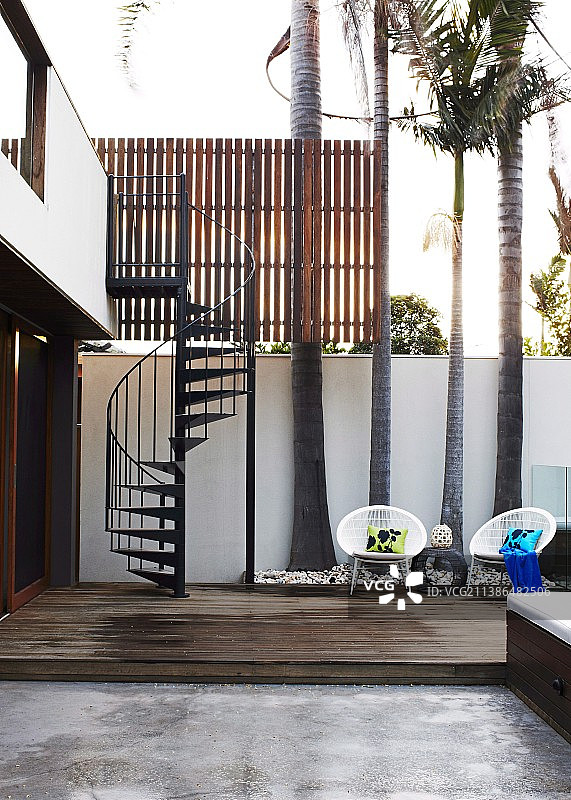 现代住宅的时尚庭院，棕榈树和螺旋楼梯前木制平台上摆放着白色柳条椅图片素材