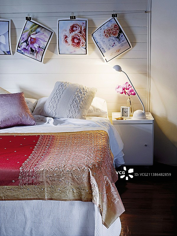 简易床上的床罩，白色木墙上悬挂着夹着的花卉照片图片素材