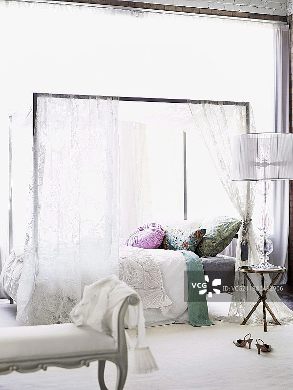 浪漫装饰的双人床与现代帷幔，前景为古董风格卧室长椅图片素材