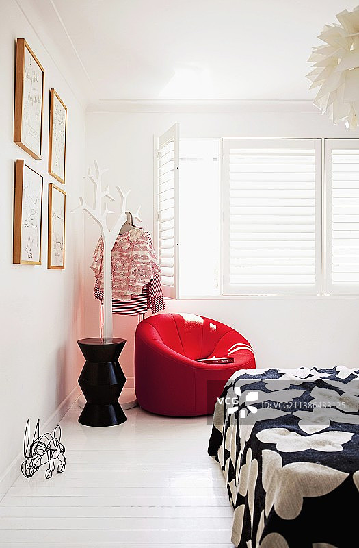 白色卧室角落里，红色软垫扶手椅旁有用作衣架的程式化树木，配有白色室内百叶窗图片素材