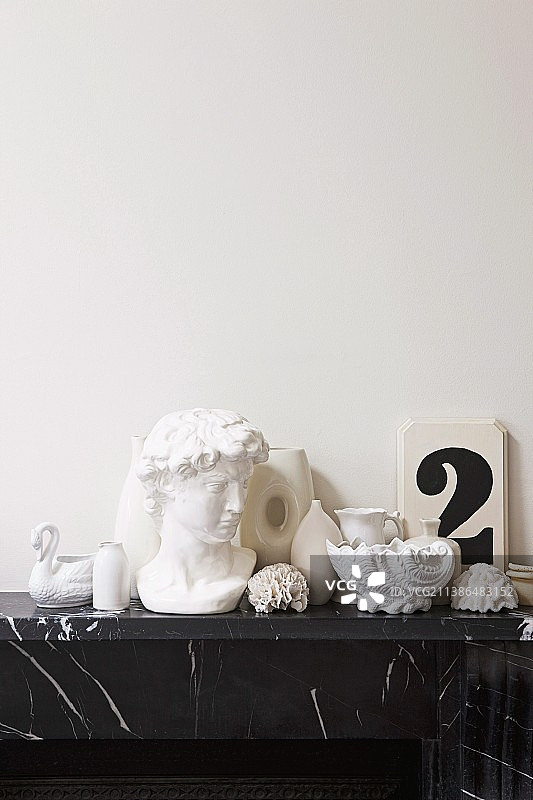 黑色大理石壁炉架上的白色装饰品，如希腊半身像、贝壳和花瓶图片素材